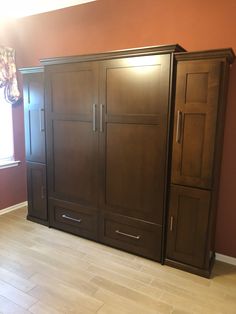 an empty room with two large wooden cupboards in the corner and a window on the far wall