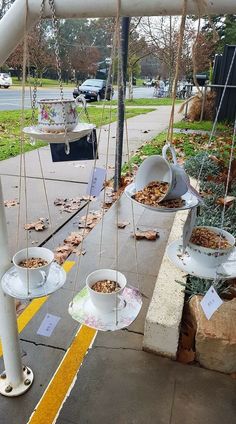 three hanging teacups filled with food on a sidewalk