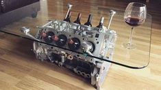 a glass table topped with an engine block and wine glasses next to it on top of a hard wood floor