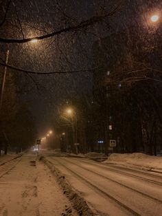 a snowy street at night with lights on and snow falling all over the road in front of it