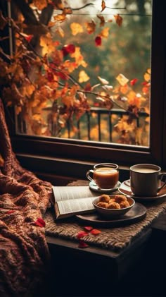 two cups of coffee sit on a table next to a window with autumn leaves outside