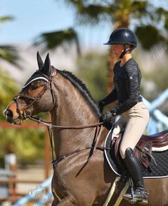 a woman riding on the back of a brown horse in an equestrian competition wearing a black helmet