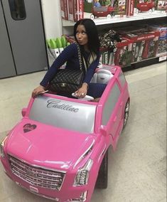 a woman standing next to a pink toy car