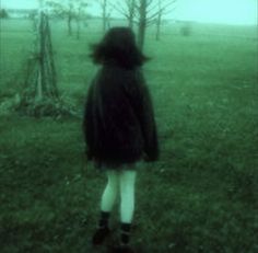 a woman standing in the grass with her back to the camera, looking at trees