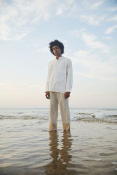 a man standing in the water at the beach with his head turned to the side