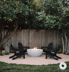 a fire pit surrounded by lawn chairs in a back yard with lights on the trees