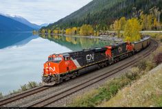 a train traveling down tracks next to a body of water with mountains in the background