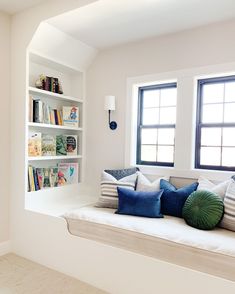 a window seat with pillows on it in front of two windows and bookshelves