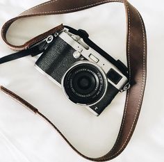 an old camera sitting on top of a white bed next to a brown leather strap