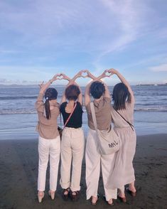 four women are standing on the beach making a heart shape with their hands while holding onto each other