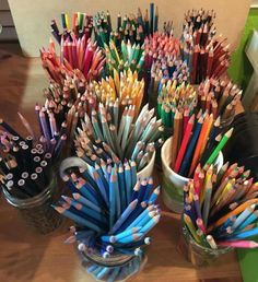 several cups with pencils in them sitting on a table next to other containers filled with colored pencils