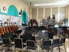 an empty classroom filled with lots of desks and chairs next to guitars on the wall