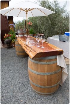 two wine glasses sitting on top of a wooden barrel with an umbrella over it's head