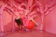 a girl is on a swing in front of pink paper trees and red ballons