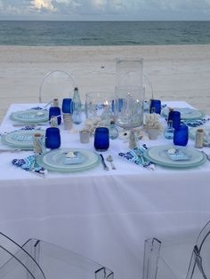 a table set up on the beach for an ocean themed dinner with blue glassware