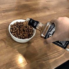 a person is pouring dog food into a white bowl on a wooden table with a bottle