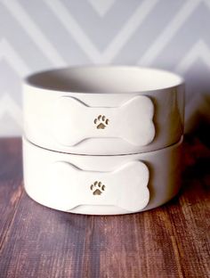 two white dog bowls sitting on top of a wooden table