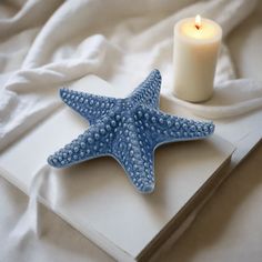 a blue starfish sitting on top of a white book next to a lit candle