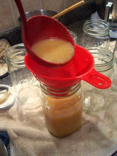 a red measuring spoon with liquid in it on top of glass jars filled with food