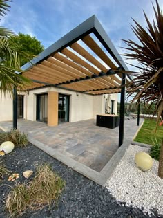 an outdoor patio with a pergolated roof and stone flooring, surrounded by palm trees