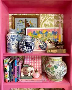 a pink book shelf filled with books and vases