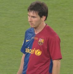 a man standing on top of a soccer field wearing a red and blue shirt with the word barcelona written on it