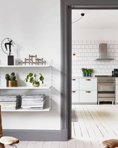 a kitchen with white walls and flooring has plants on the shelves above the stove