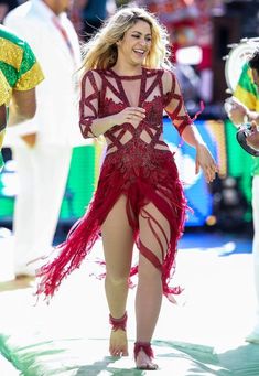 a woman in a red dress is dancing on the stage with other people behind her