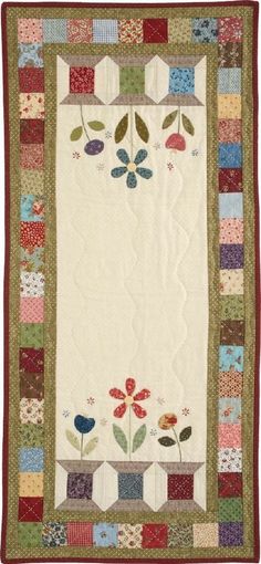 a quilted wall hanging with flowers and leaves in the center, on a white background