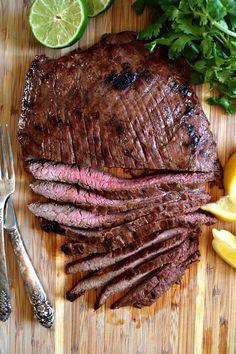 the steak is sliced up and ready to be served with lemons, parsley and herbs