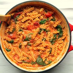 a red pot filled with pasta and spinach on top of a white countertop