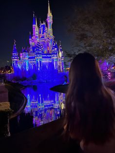 a woman is looking at the castle lit up in purple and blue colors with lights on it