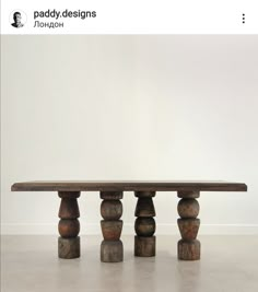 a wooden table sitting on top of a cement floor next to a white wall and two black vases