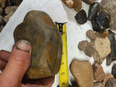 a person holding a rock with a measuring tape on it next to rocks and stones