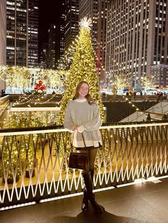 a woman standing on a balcony next to a christmas tree in the city at night