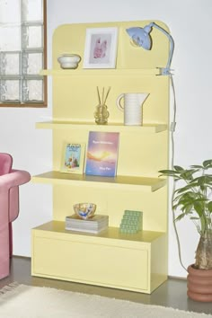 a yellow book shelf with pictures and books on it next to a potted plant