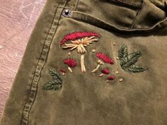 an embroidered green jacket with red flowers and leaves on the front, sitting on a wooden surface