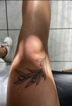 a woman's leg with an olive branch tattoo on her left side ribcage