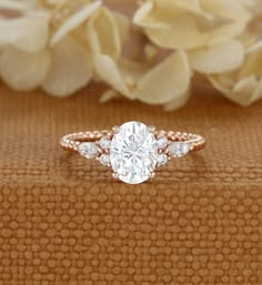 an oval cut diamond engagement ring with two side stones on the band and a flower in the background