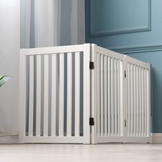 a white baby crib next to a blue wall and potted plant on the floor