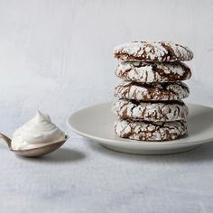 a white plate topped with cookies covered in powdered sugar next to a bowl of whipped cream