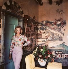 a woman standing in front of a painting on the wall next to a yellow chair