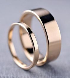 two gold wedding rings sitting on top of each other in front of a blue cloth