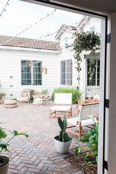 an open patio with potted plants and seating on the brick floor, next to a white house