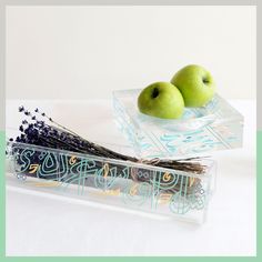 two green apples sitting on top of a glass container next to lavender and an apple