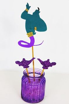 a purple vase filled with cake toppers sitting on top of a table