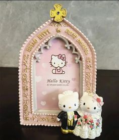 two hello kitty figurines sitting next to each other on a table with an ornate frame