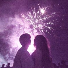 two people standing in front of a fireworks display with their backs to the camera, facing each other