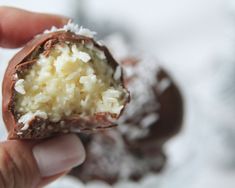 a hand holding a half eaten chocolate and coconut truffle with powdered sugar on top