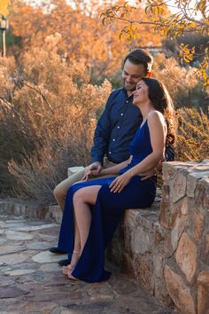 a man and woman sitting next to each other on a stone wall